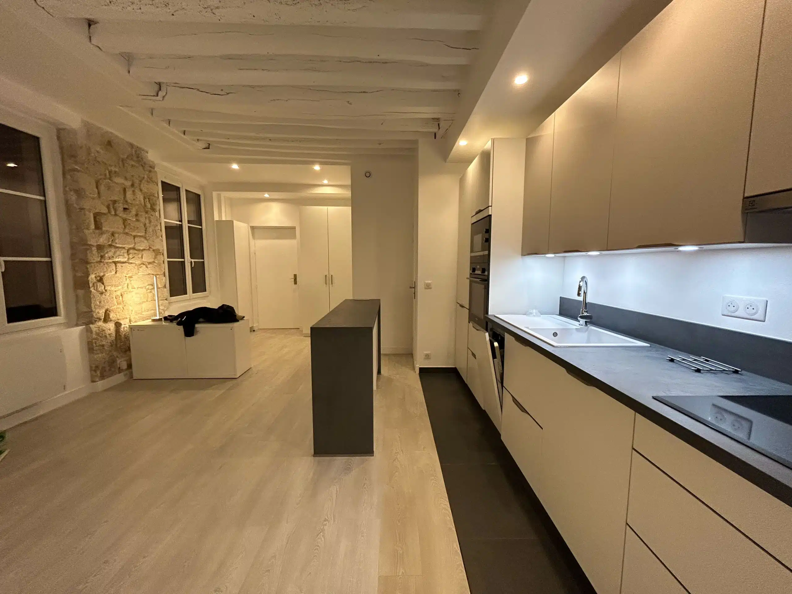 Séjour et cuisine ouverts dans un appartement ancien parisien, poutres apparentes au plafond