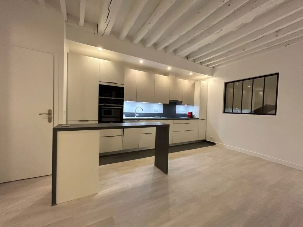Cuisine ouverte sur le séjour avec verrière atelier et poutres apparentes peintes, appartement parisien rénové